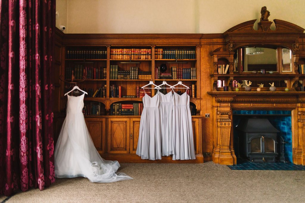 A bride's wedding dress hangs on a hanger beside 3 bridesmaids dresses