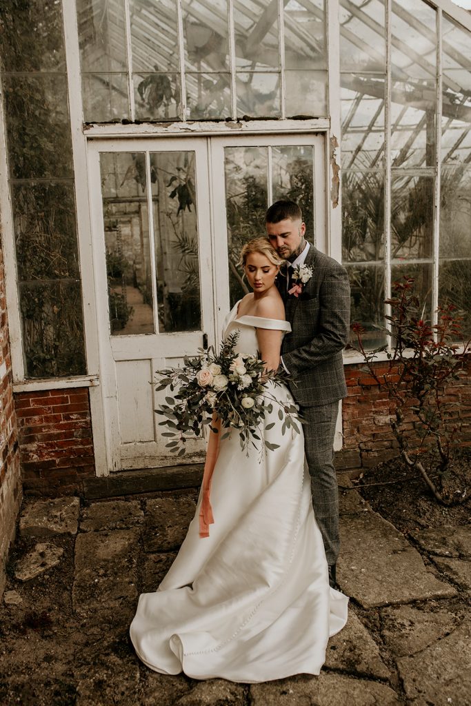 A tender embrance for newlyweds outside a rustic greenhouse
