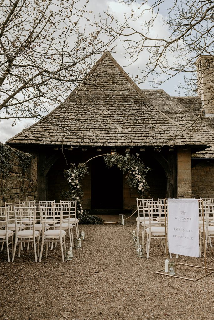 Outdoor ceremony settin with cream chivari chairs and aisle styled with candles with dramatic foliage covered moongate arch