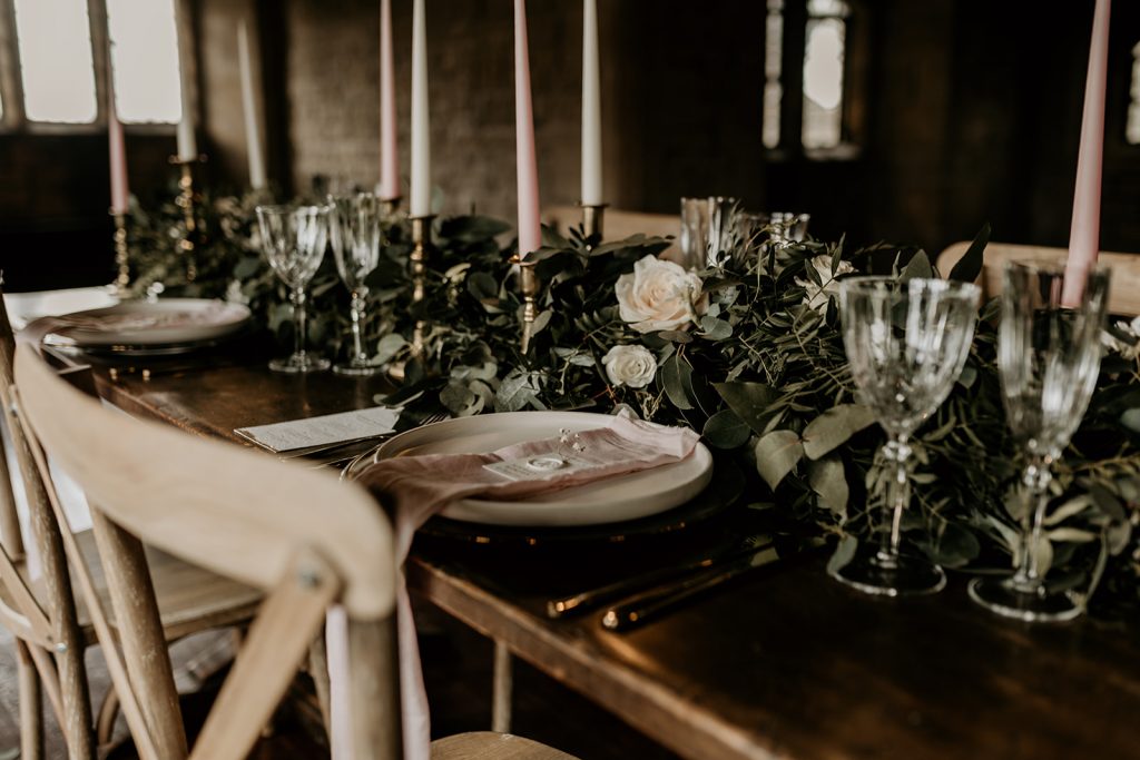 View of top banqueting style wedding table with rustic styled central green garland and exposed wooden tables and chairs