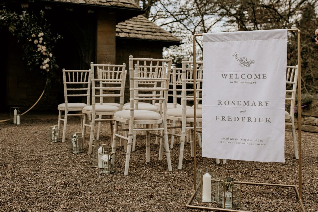 Wedding welcome sign for wedding ceremony on cream textured fabric hung from gold frame
