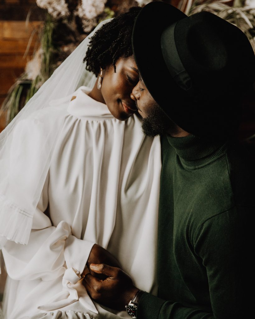 Newlywed bride and groom in a tender embrace. The bride wears a high neck long sleeved Moonchild wedding dress with a veil
