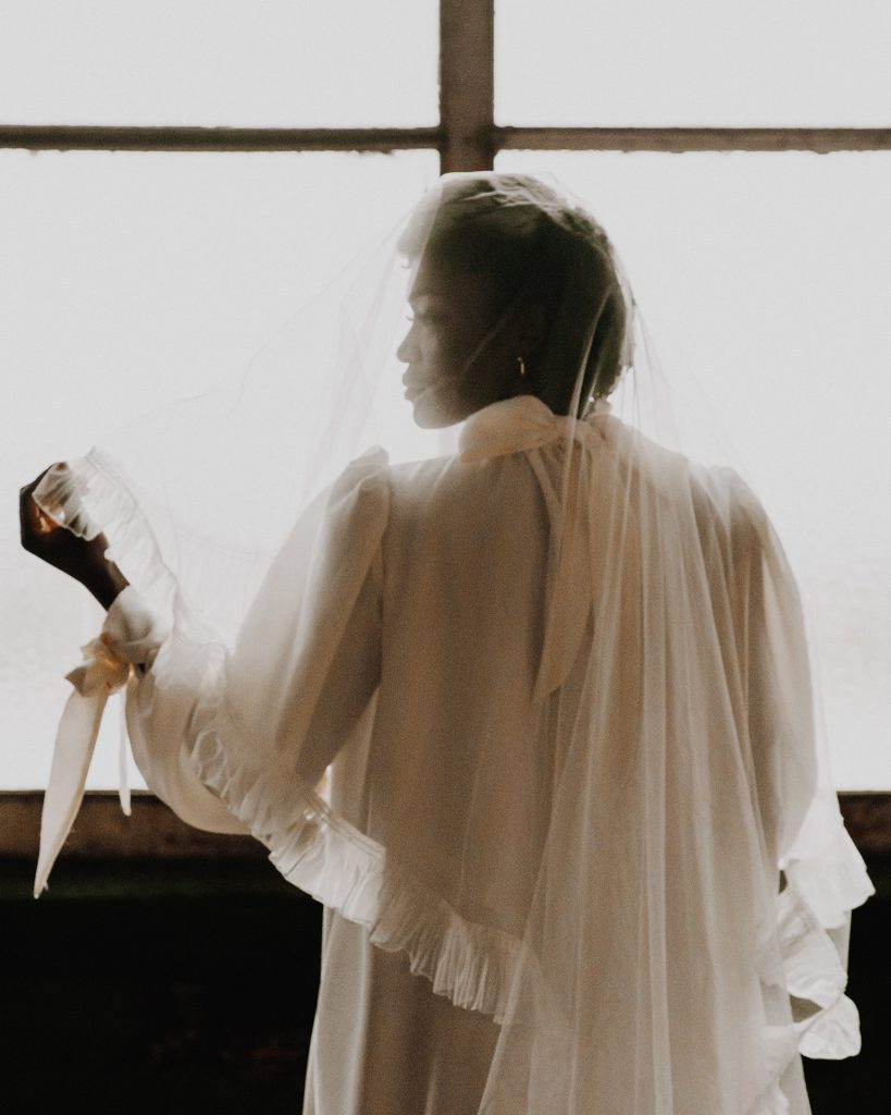 Back of a bride's wedding dress with a veil over her face. She wears a long sleeve Moonchild wedding dress