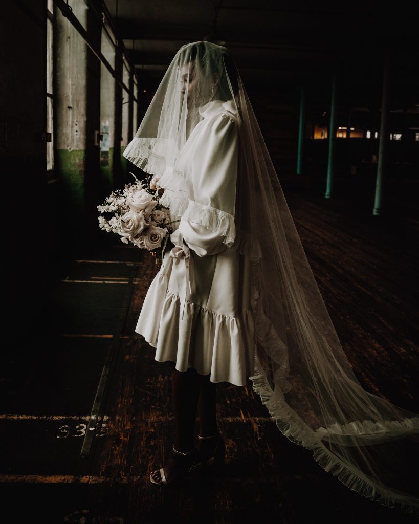 Bride in short Moonchild wedding gown with long Cathedral length veil and muted tone wedding bouquet