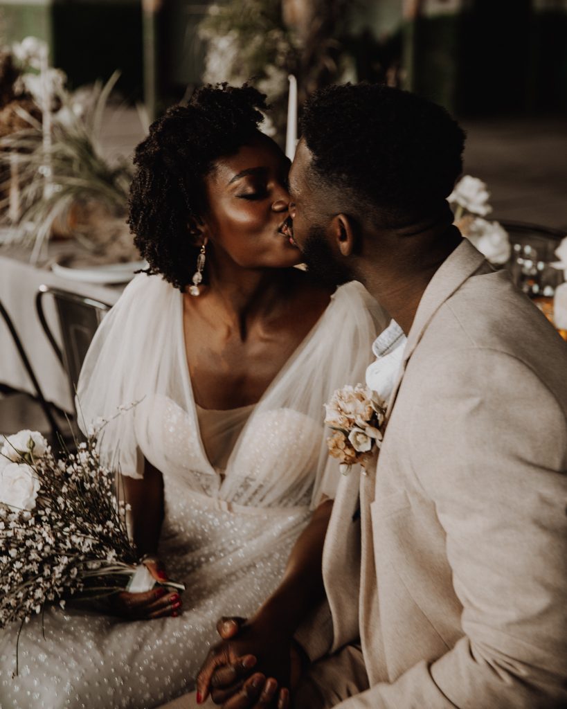 Newly married bride and groom share a gentle kiss. The bride wears a beautiful Berta wedding gown and holds a white wedding bouquet