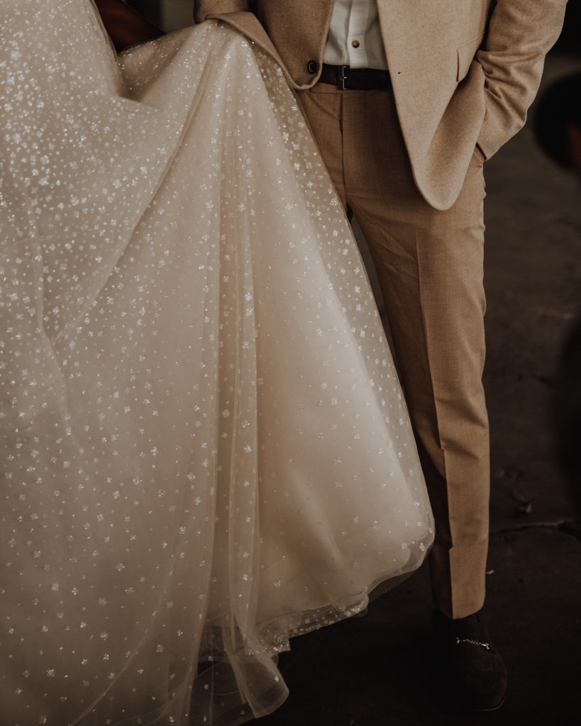 Close up image of bride's sparkling Berta wedding dress held by her Groom at their micro wedding