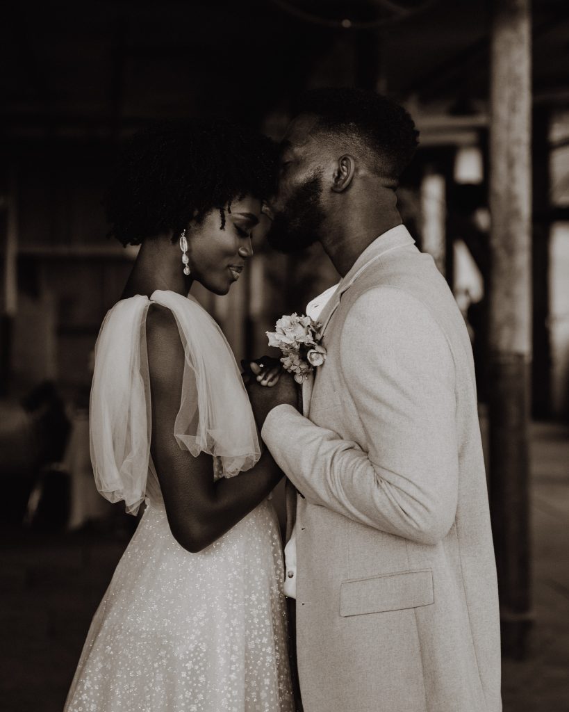 Bride and groom gently embrace. He wears a tan coloured suit and the bride wears a beautiful sparkling Berta wedding dress