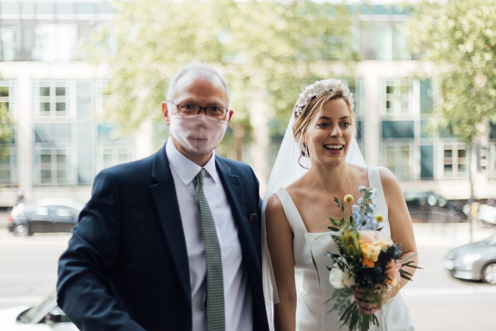 Father of the bride with face mask about to walk his daughter down the aisle for her London civil ceremony