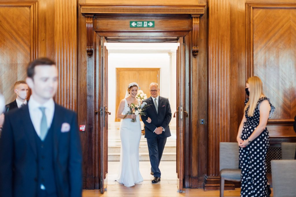 Brid wearing sleeveless fitted wedding dress with flower crown and long veil about to walk down the aisle