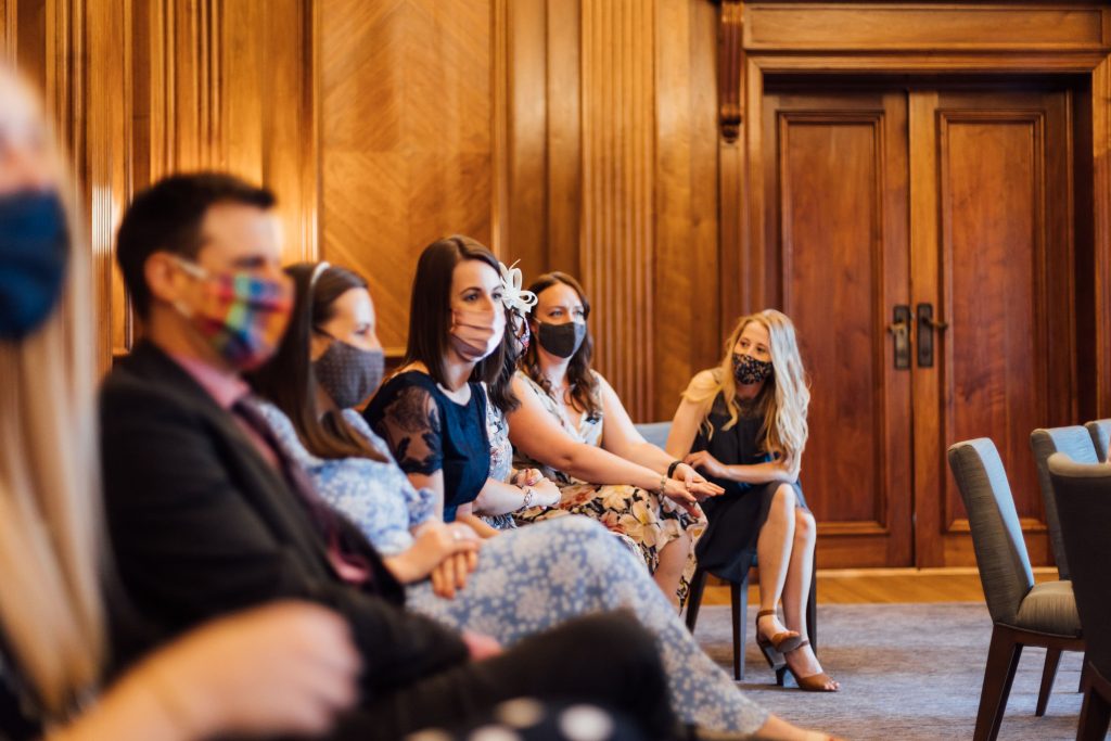 Guests of city micro wedding couple sit in ceremony room wearing face masks