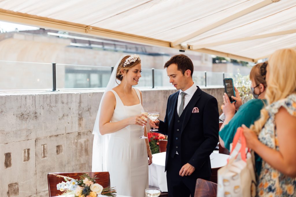 Bride in sleeveless summer wedding dress and flower crown with veil toasts to her new husband