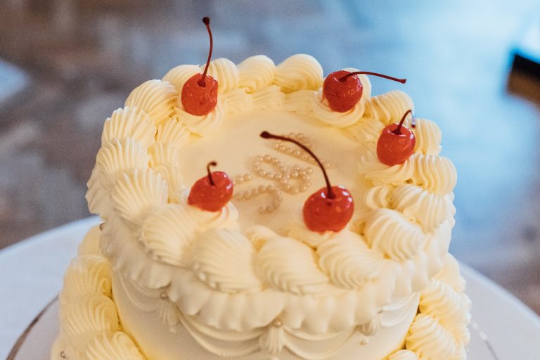 Two tier cream wedding cake with piped detailing and charry topping for low key summer micro wedding