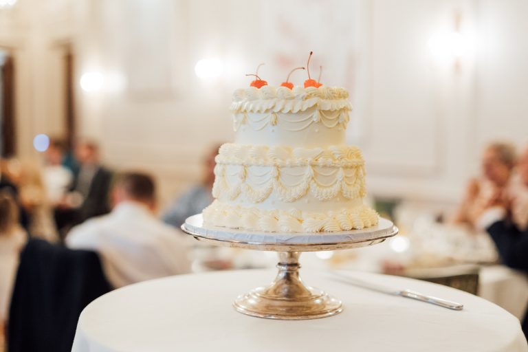 Two tier cream wedding cake with piped detailing and charry topping for low key summer micro wedding