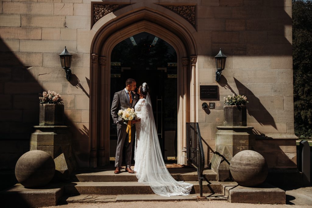 A bride and groom stand at the front entrance of their grand country manor house wedding venue