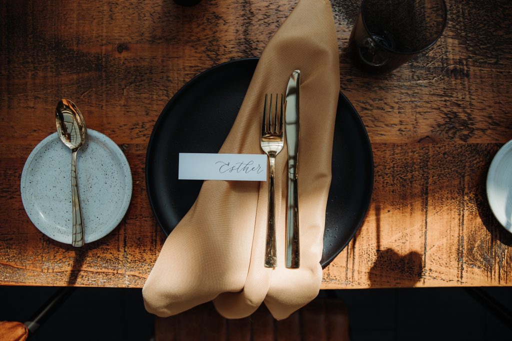 Close up of wedding place setting of a charger plate, cutlery, name card and a napkin on top of a wooden table