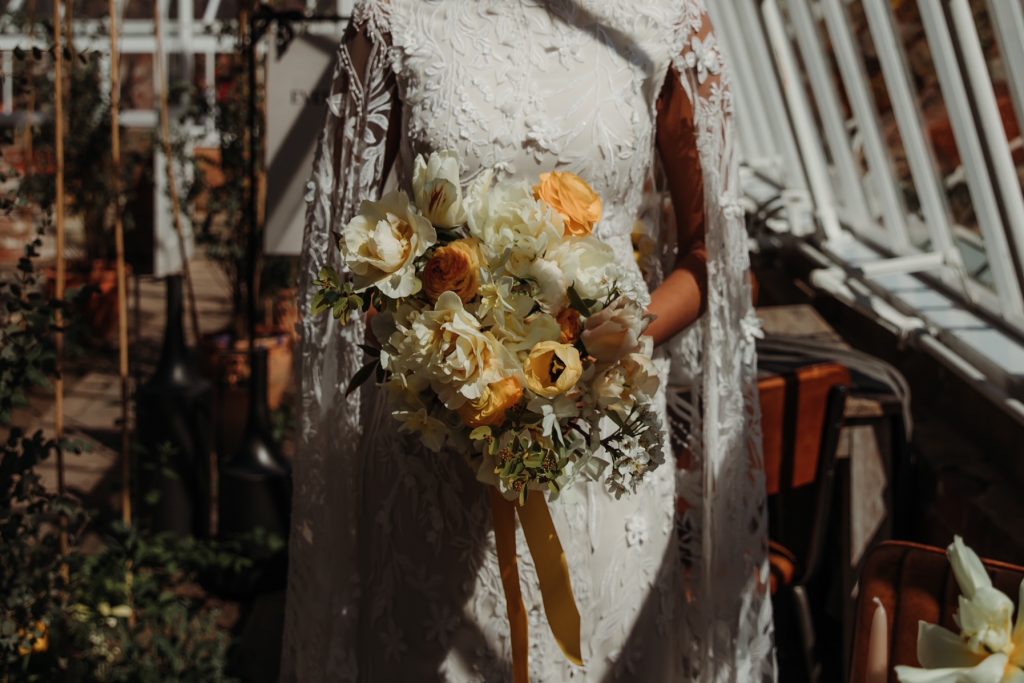 Close up of a wedding bouquet of soft yellows and creams. The bride wears an intricate hand embroidered white wedding dress