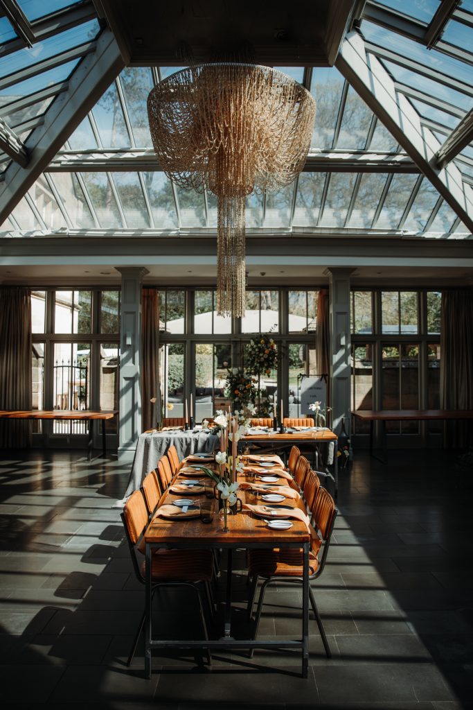 Glass house wedding venue with contemporary exposed wooden table styling