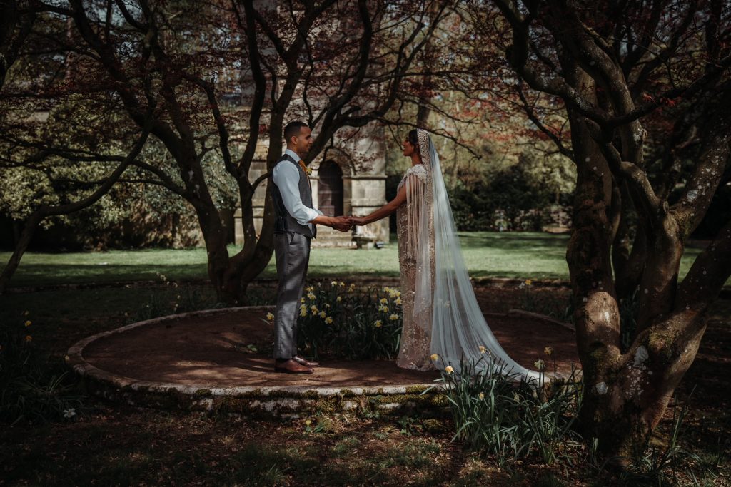 A wedding couple stand holding hands under the acer trees at their country house wedding venue