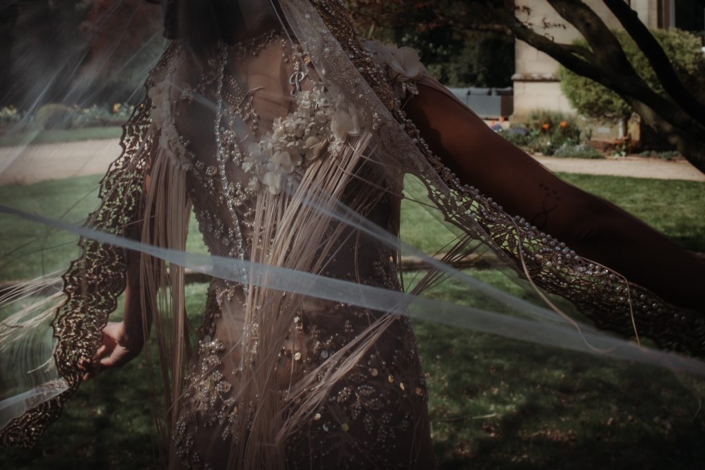 A close up of the back of a bride wearing a hand beaded wedding dress with a sheer veil blowing in the wind
