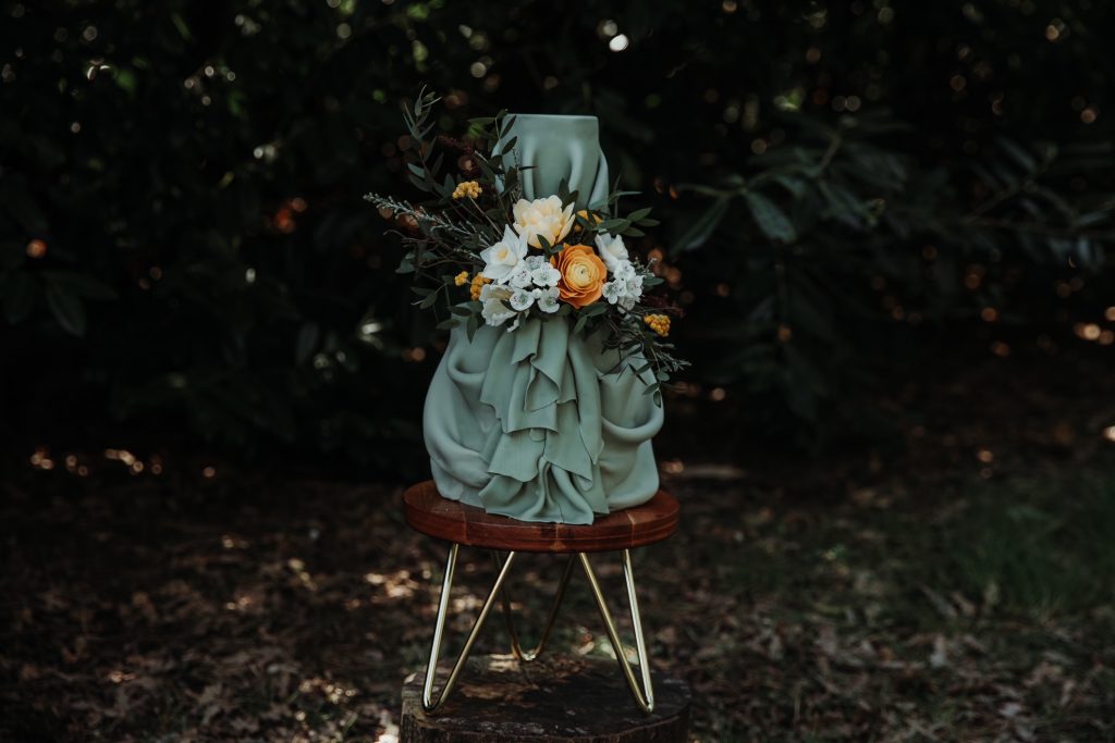 A green drape wedding cake covered in fresh flowers on a wooden stand