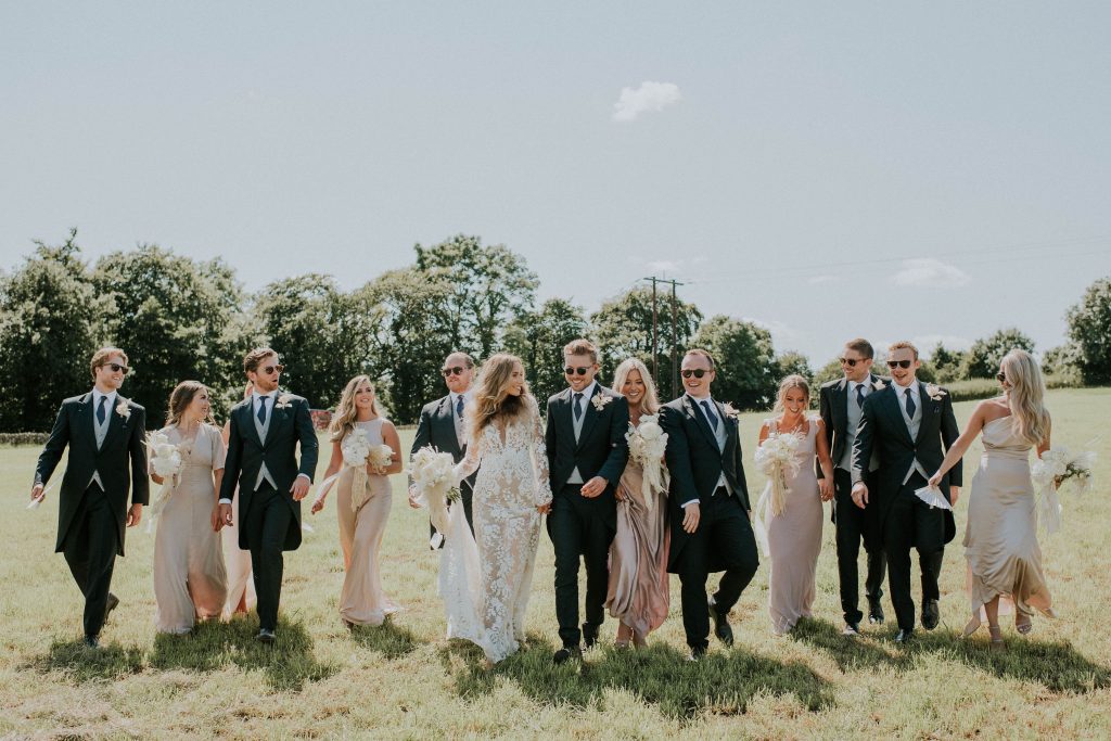 Bride and groom with wedding party outside in the field at their summer barn wedding