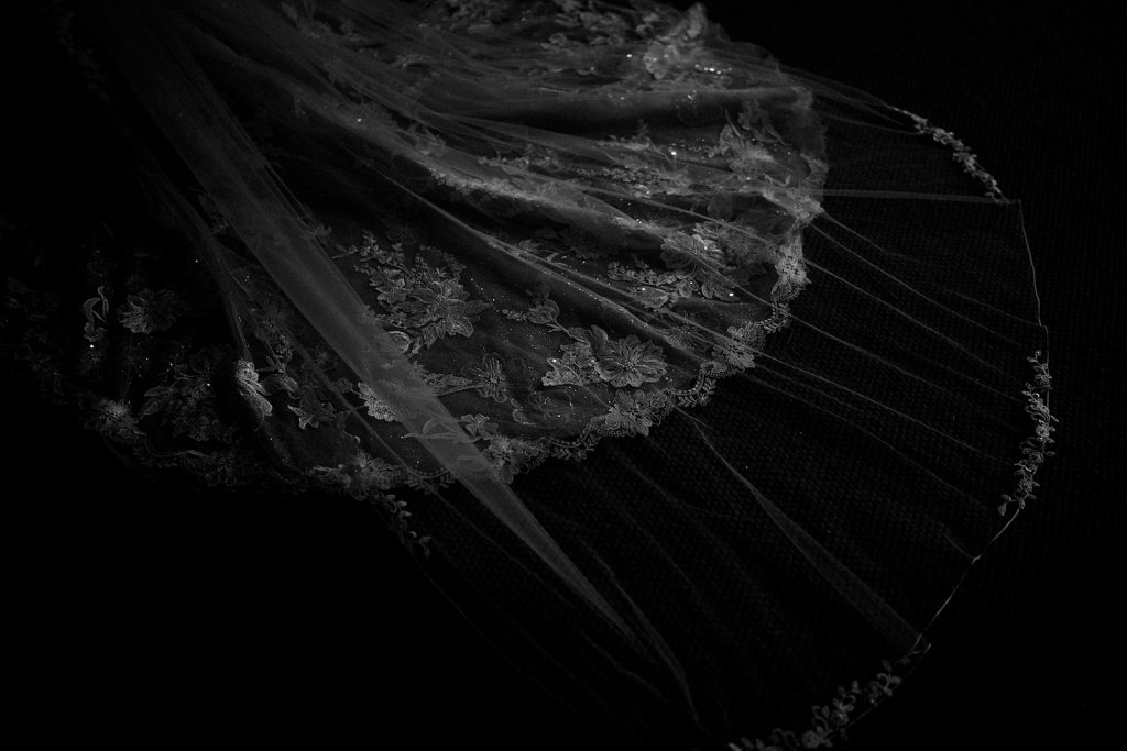 Close up black and white image of the intricate lace detailing on the bottom of an Enzoani wedding dress train