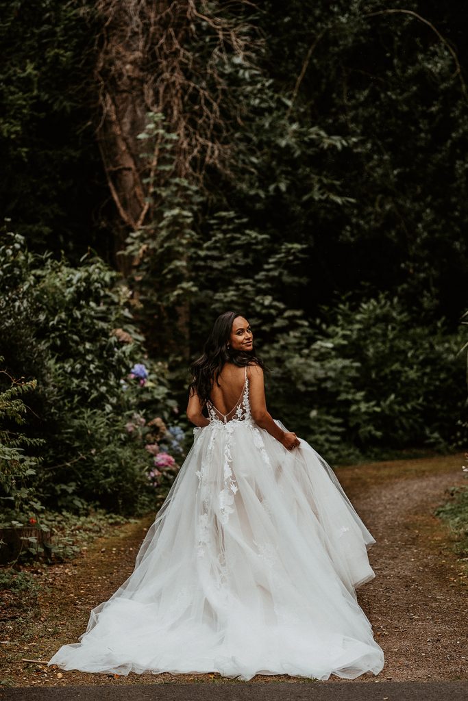 Back shot of bride in an Enzoani wedding dress as she walks through the gardens of her country house wedding venue