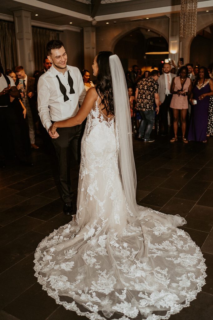 A bride in an Enzoani wedding dress stands on the dance floor with her new husband with his bow tie undone