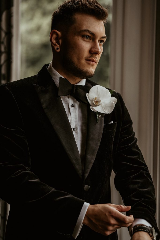 A groom dressed in his black tie wedding attire with a fresh white orchid button hole