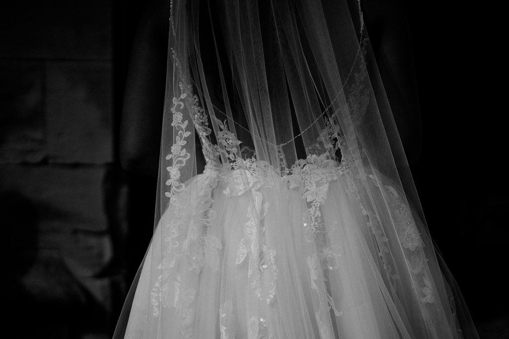 Close up black and white image of the detailed lace design of a bride's Enzoani wedding dress with a long veil