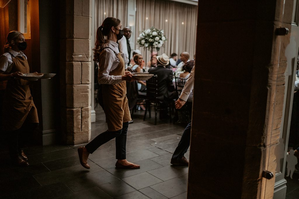 Waiting staff wearing face masks serve food during the wedding breakfast in a country manor house venue