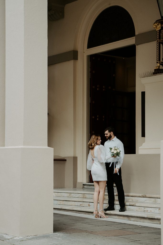 A bride in a short wedding dress embraces her new husband in London city during their intimate wedding day