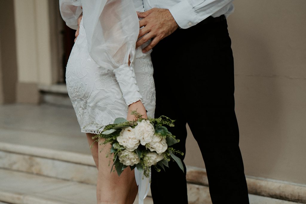 Close up of a short wedding dress for city elopement bride, embraced by her husband