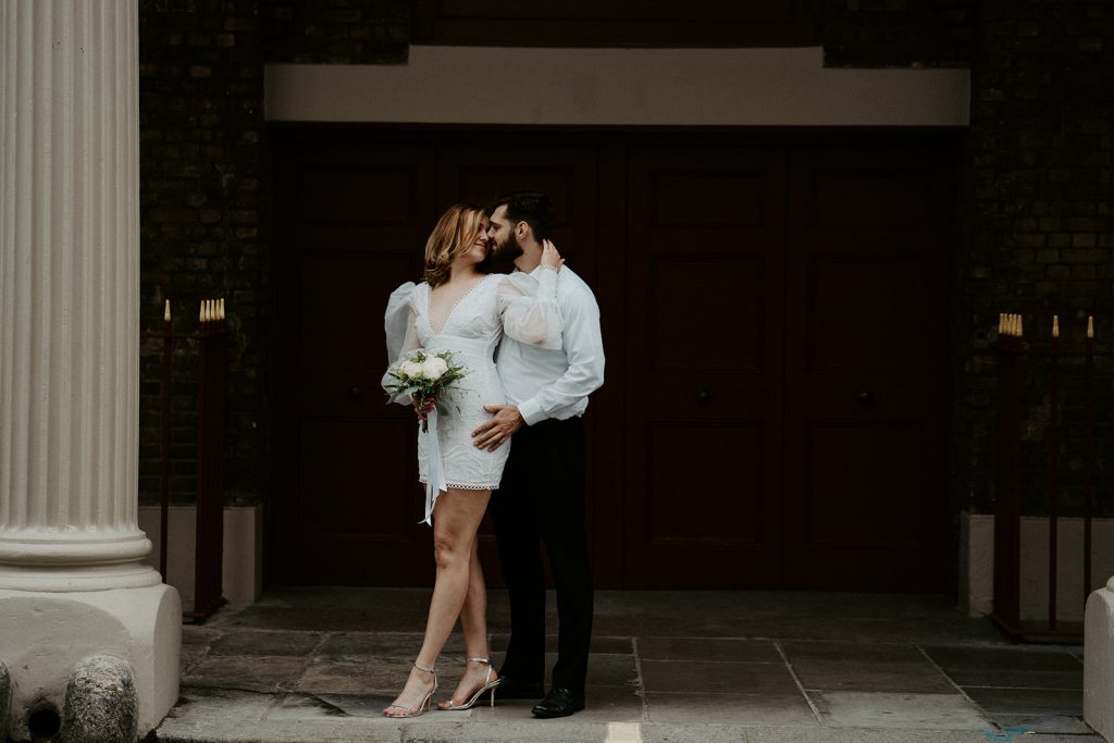 Bride in a short wedding dress caresses her husband's face gently as he hold her around the waist