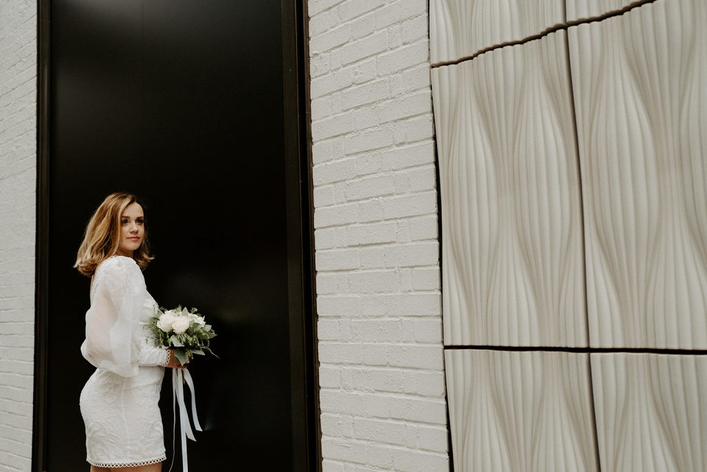 POrtrait of bride on her wedding day in a short wedding dress holding a bouquet of flowers