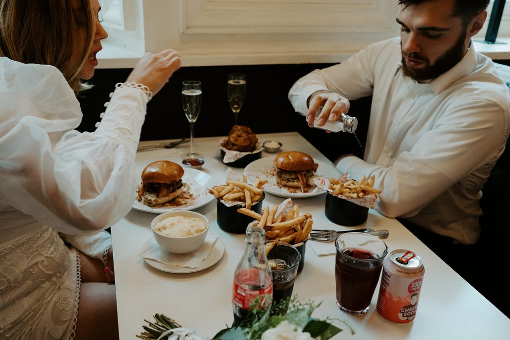 Newly married bride and groom enjoying burgers, fries and Champagne during their city elopement