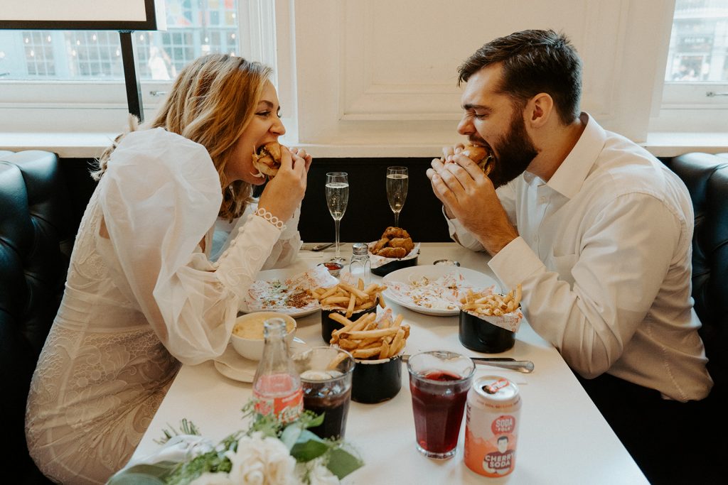 Newly married bride and groom enjoying burgers, fries and Champagne during their city elopement