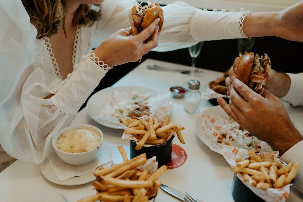 Newly married bride and groom enjoying burgers, fries and Champagne during their city elopement