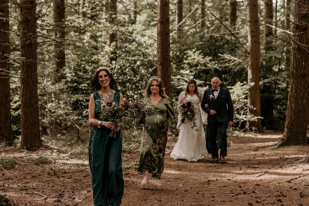 Bridesmaids in green dresses walk down the aisle ahead of the bride and her father just before her wedding ceremony