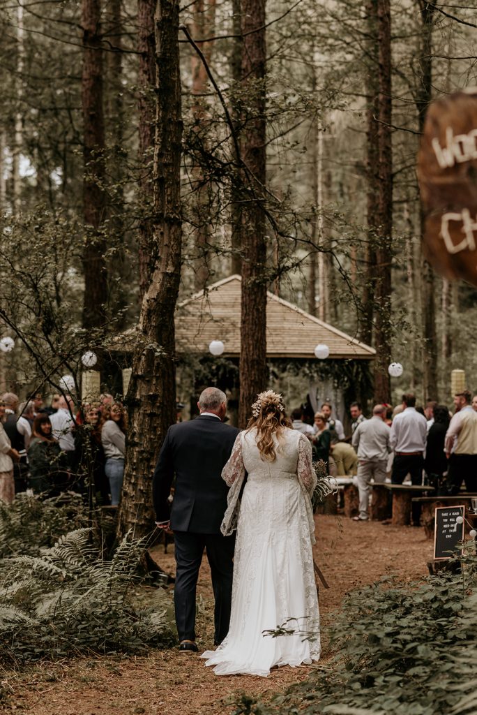 A bride in a lace bespoke wedding dress walks up the aisle with her father on her wedding day