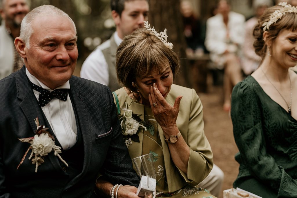 A guest becomes overcome with emotion and wipes away tears during heartfelt woodland ceremony