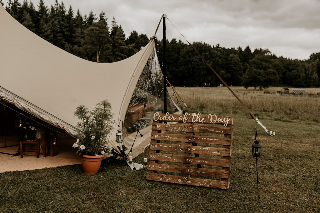 DIY wooden order of service palette outside marquee tent for boho wedding