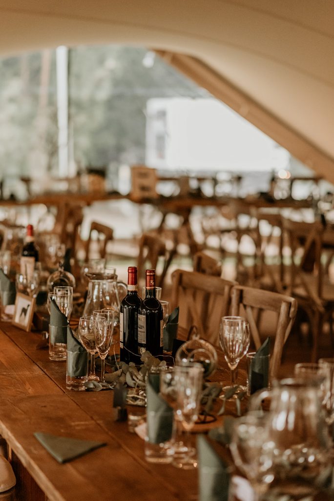 Rustic banquet wooden tables set up for marquee wedding with wooden chairs