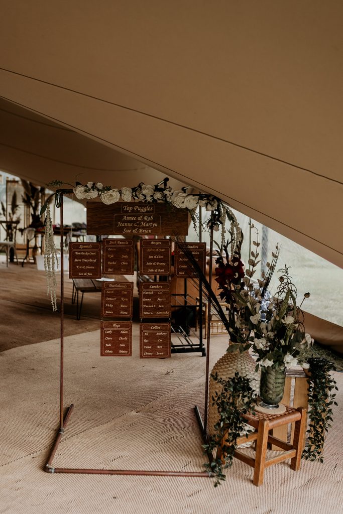 Wooden wedding table plan hanging from frame inside marquee for boho wedding