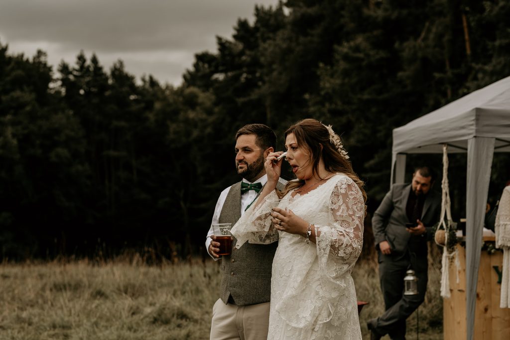 A bride wipes away a tear during emotional outdoor speeches on wedding day