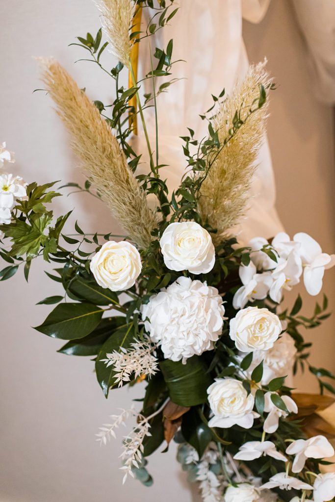 Close up of a wedding moongate featuring pampas, orchids, white roses and a touch of green foliage