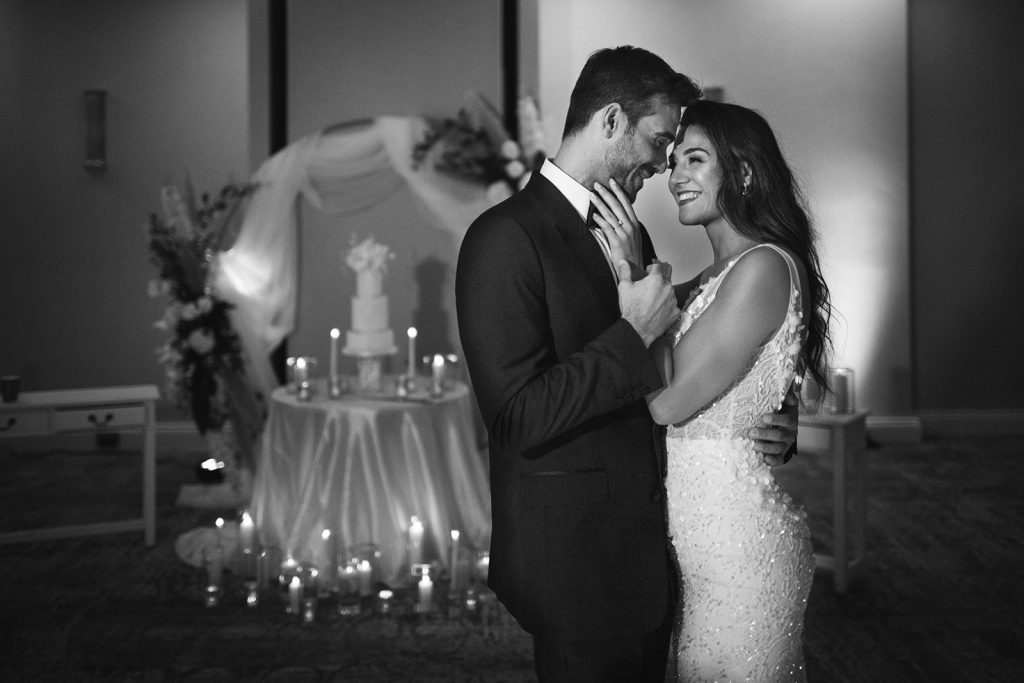 A black and white image of a wedding couple having their first dance in front of their wedding cake display