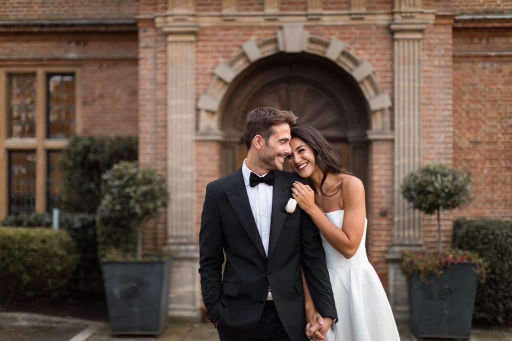 Groom in black tie wedding attire and bride in Mirror Mirror London Couture gown hold hands on their wedding day