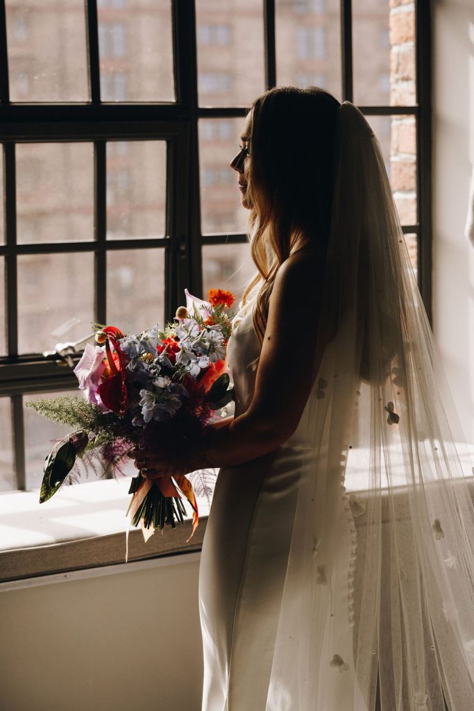 A modern bride in a contemporary Suzanne Neville wedding gown and long veil reflects and takes a moment on her wedding morning