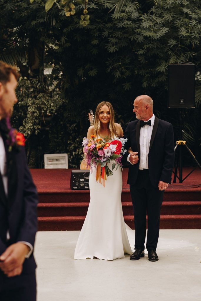 A father about to walk his daighter up the aisle on her wedding day as her soon to be husband gets his first look at his bride